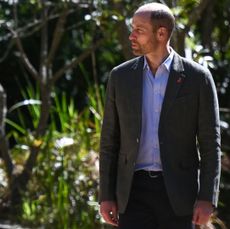 Prince William wearing a gray blazer and pants walking in the woods