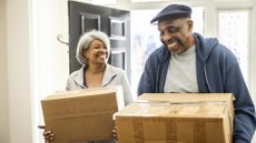 An older couple carry moving boxes into their new home.