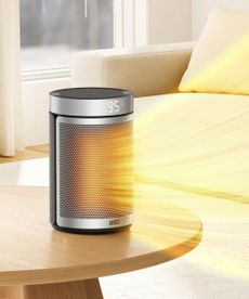 Dreo Portable 1500W Fast Ceramic Space Heater on coffee table with orange rays coming out representing heat, against beige sofa in living room