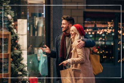 couple wrapped up in coats and hats looking in a shop window while Christmas shopping