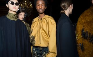 Models wear yellow blouse with dark blue coat and skirt and black hexagonal sunglasses.