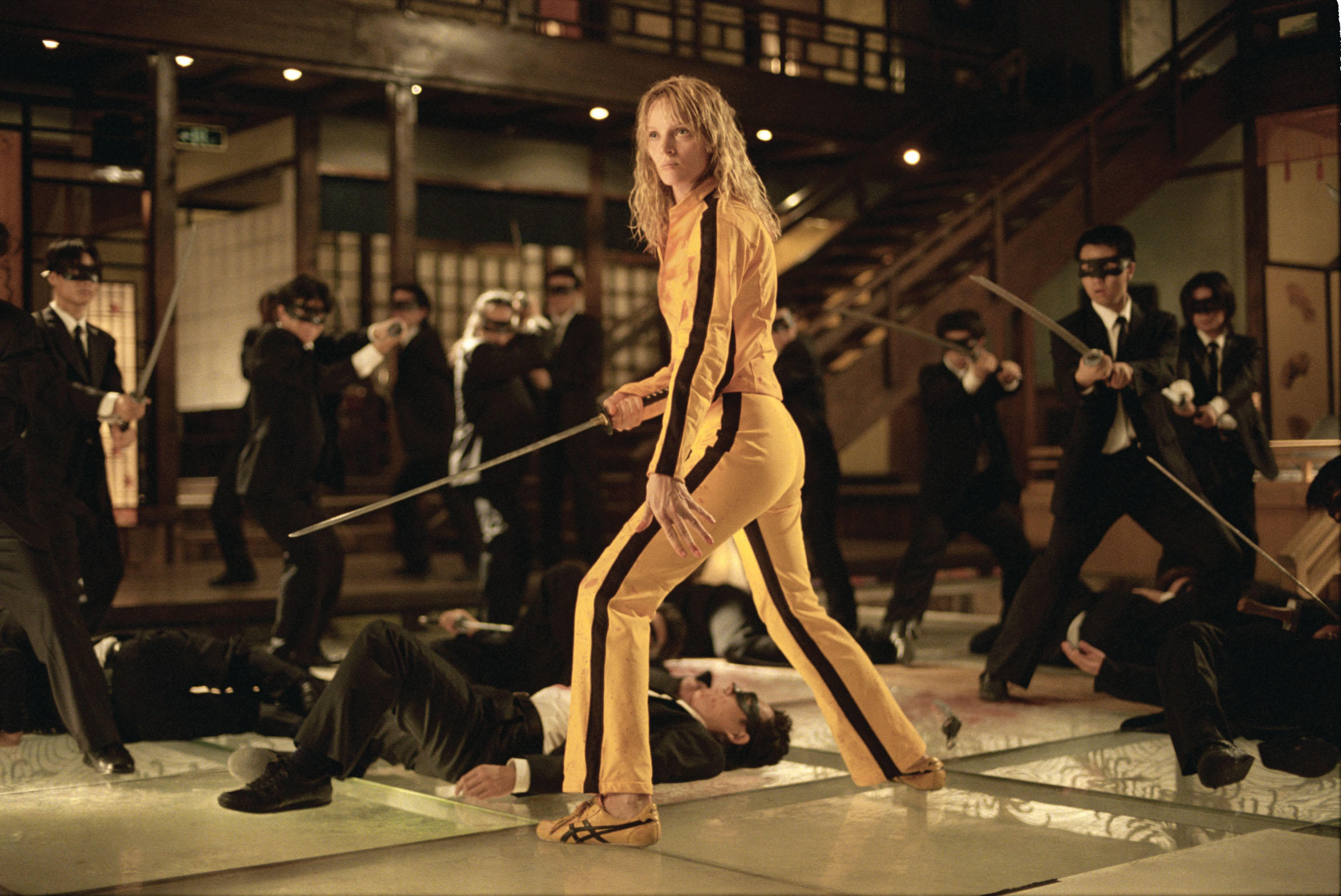 Uma Thurman como La Novia, con un mono amarillo y sosteniendo una espada, está rodeada por los locos 88 Yakuzas en Kill Bill Vol. 1