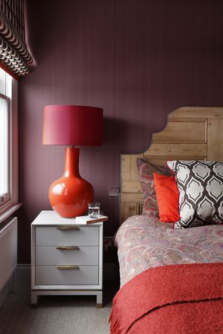 Dark purple bedroom with red lamp and headboard