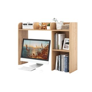 A multi-tier wooden desktop bookshelf with a Mac screen below and a bunch of books on the shelves