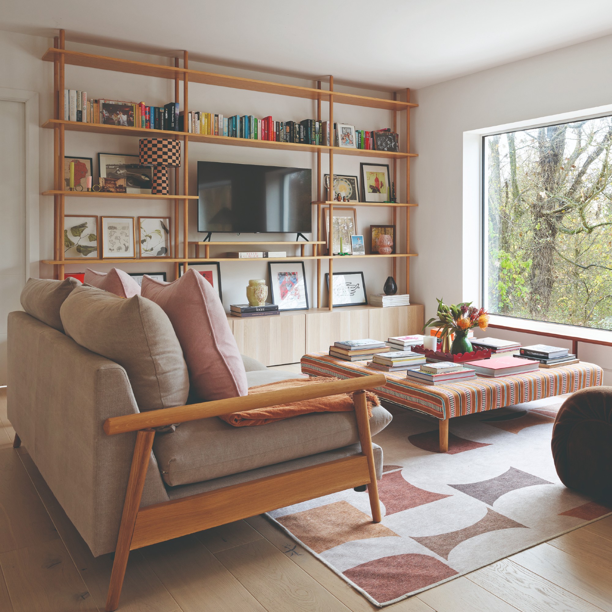 A living room with Scandi-style wooden open shelving housing the TV and a large patterned ottoman used as a coffee table