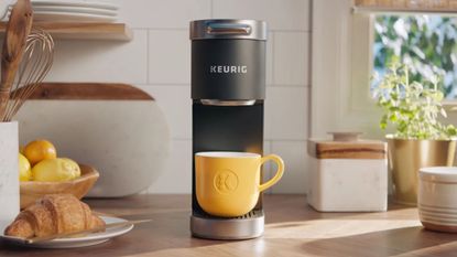 A Keurig K-Mini single Serve Coffee Maker in a modern Kitchen ready to pour coffee into a yellow mug