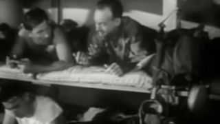 Black and white screenshot of men on bunks on a transport ship