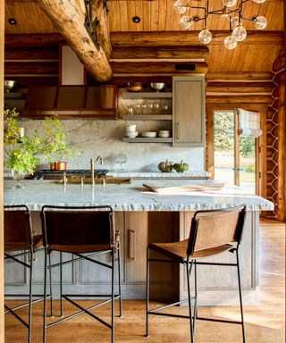 A log cabin kitchen with wood paneling on the ceiling and walls and marble countertops and backsplash