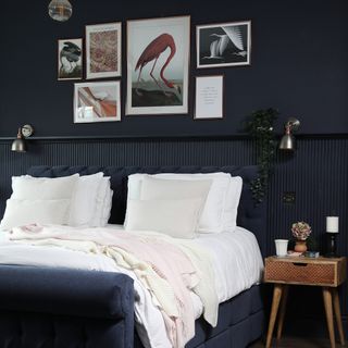 Dark painted panelled bedroom wall, navy blue bedframe, white bedding, hanging wall art, bedside table
