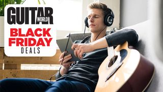 Man holding acoustic guitar listens to music through headphones