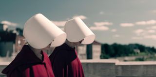 two women in white bonnets and red cloaks walking side by side in the handmaid's tale