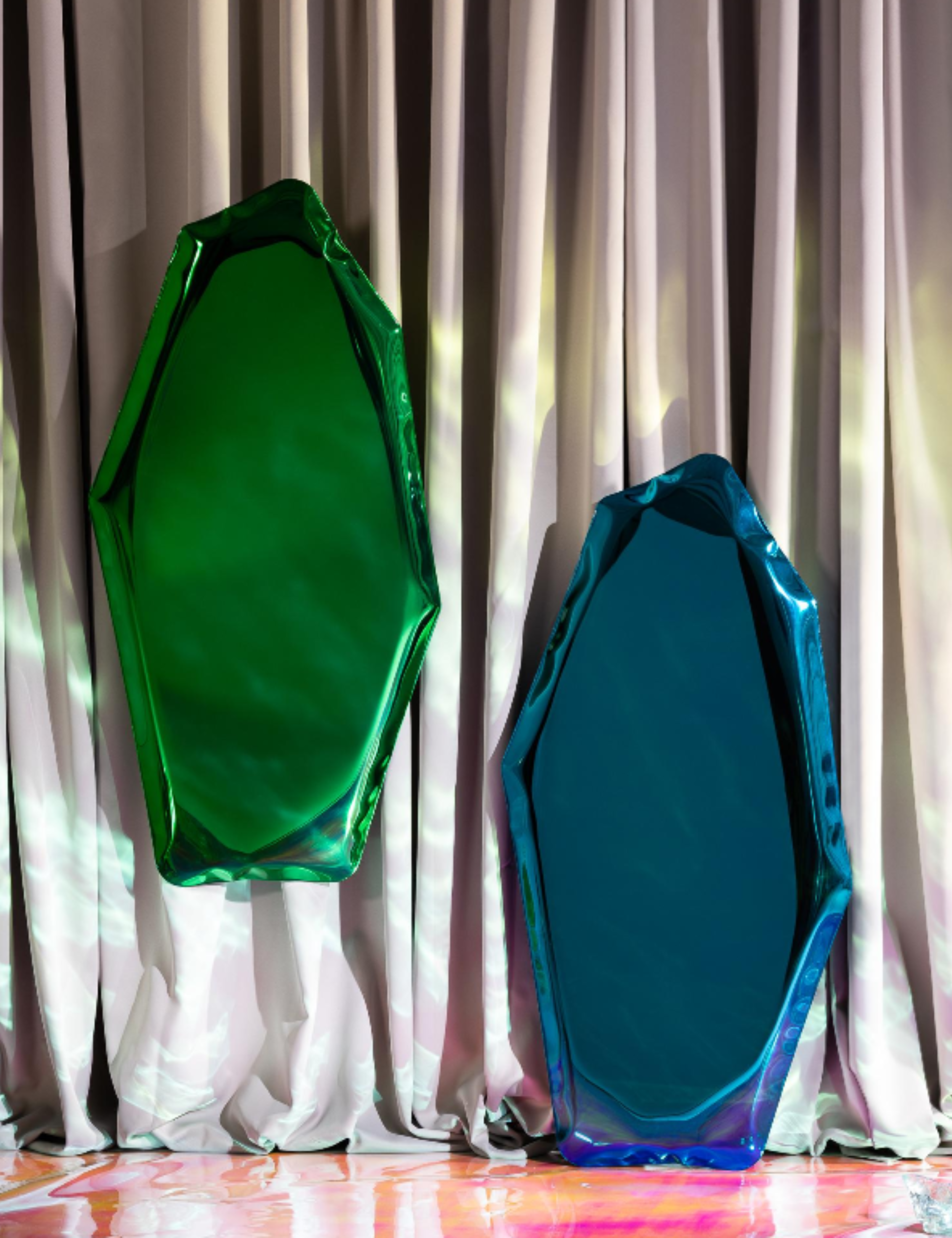 Green and blue chrome floor mirrors displayed against silvery drapery
