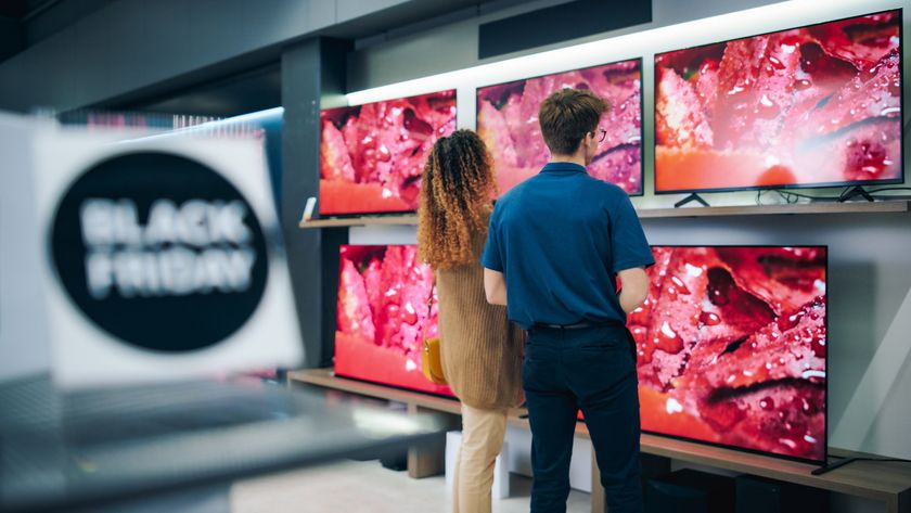Two people in a retail store standing in front of several TVs available for sale. In the foreground is a sign that reads: &quot;Black Friday.&quot;