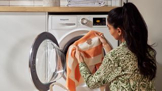 A woman putting a stained garment in a Hotpoint washing machine