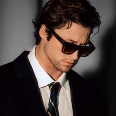 An image of "Off Campus" star Stephen Kalyn wearing sunglasses, a black jacket, a white button-down shirt, and a striped tie.