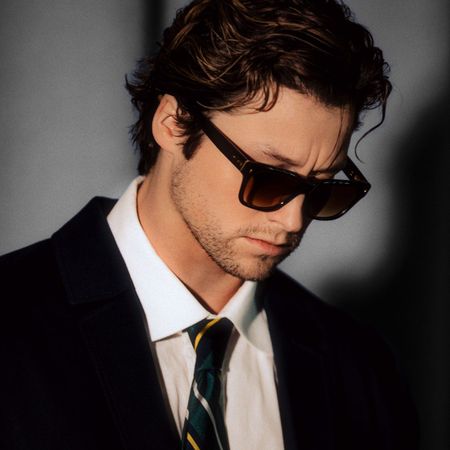 An image of "Off Campus" star Stephen Kalyn wearing sunglasses, a black jacket, a white button-down shirt, and a striped tie.