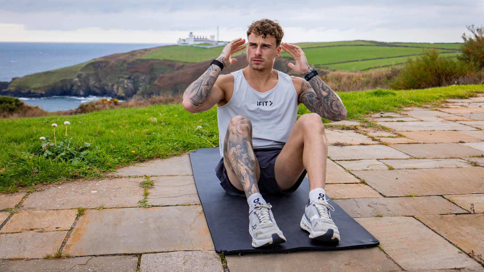 Man doing sit-up exercise outside on a patio with cliffs and the sea behind him