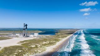 spacex's stainless steel starship rocket stands on its launch pad with the turquoise waters of the gulf of mexico nearby.