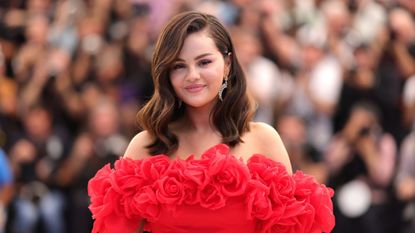 Selena Gomez with a brown bob wearing a red off the shoulder rose dress, with a row of people behind her