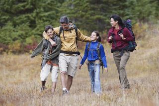 A family of four wearing backpacks and hiking through a field