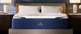 The DreamCloud Hybrid Mattress on a bed frame in a bedroom, between two night stands with lamps on top, two pillows balanced at the top end of the bed