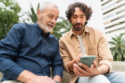 Father and adult son look at a phone.