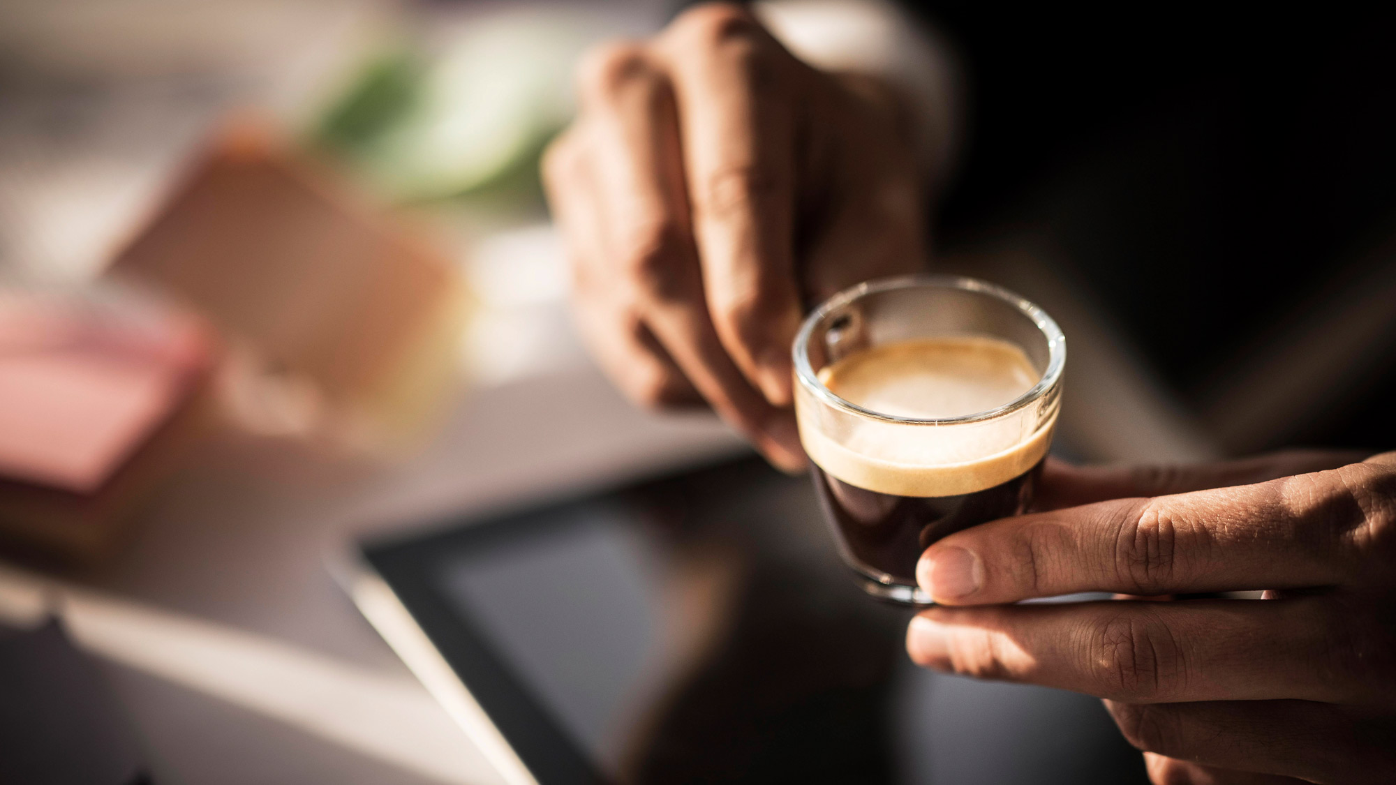An espresso in a glass cup being held by two hands