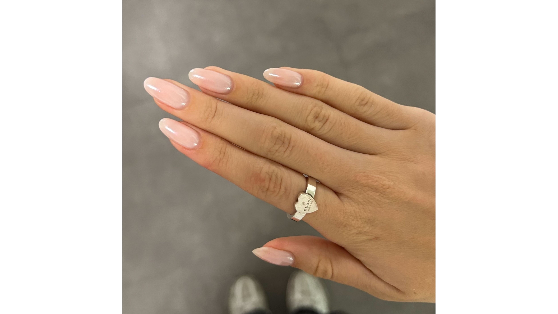 A close-up of Digital Beauty Writer, Sennen Prickett's hand, which features a pink, pearly almond manicure, pictured in front of a grey floor background