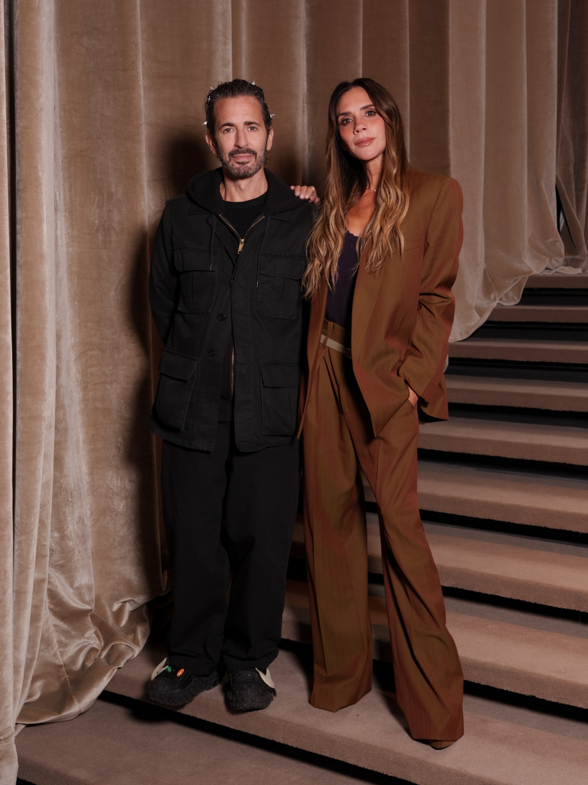 Victoria Beckham poses for a photo with Marc Jacobs wearing a brown oversized suit with a black camisole top.