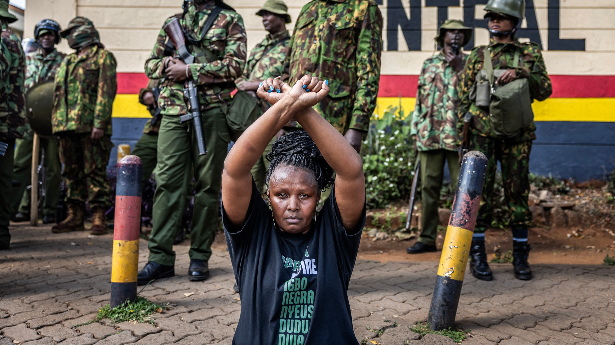 A protester sits in front of Kenyan police officers guarding the entrance to the Central Police Station in Nairobi