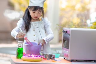 A young girl mixing food ingredients in a bowl, next to a mini-oven.