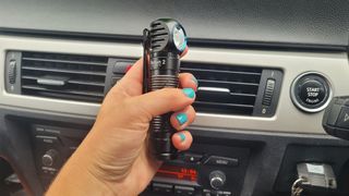 Olight Perun 2 being held in someone's hand inside a car.