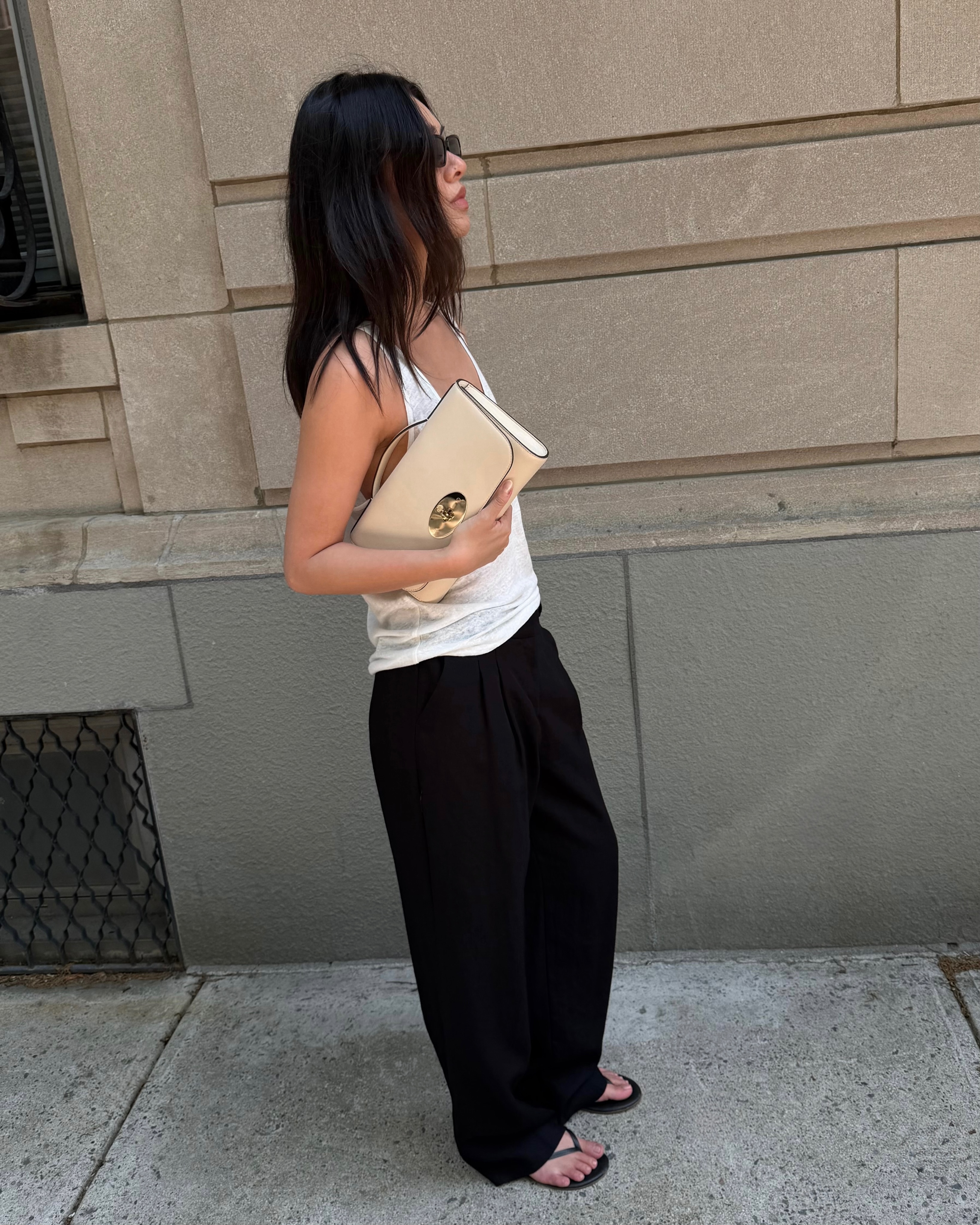 An image of an influecner in a white vest, black trousers and carrying a cream-coloured top handle clutch