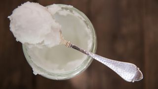 Spoonful of coconut oil resting on a tub of coconut oil.