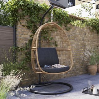 A rattan-effect hanging egg chair in the garden on a paved patio