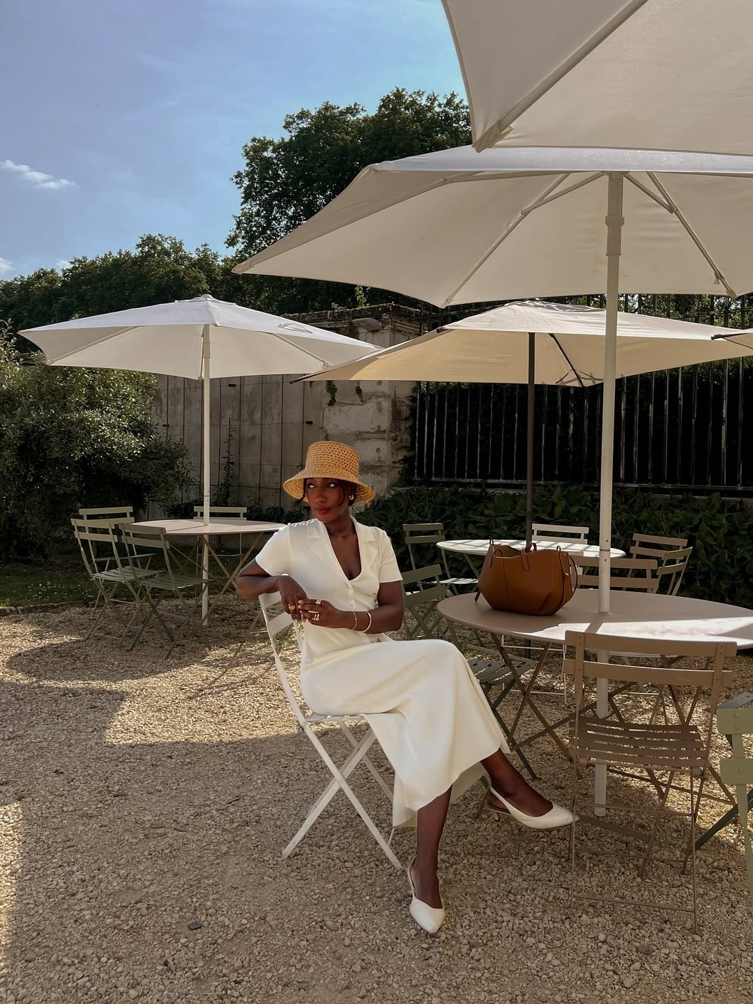 Woman wears white dress, straw hat and white shoes, and has tan bag