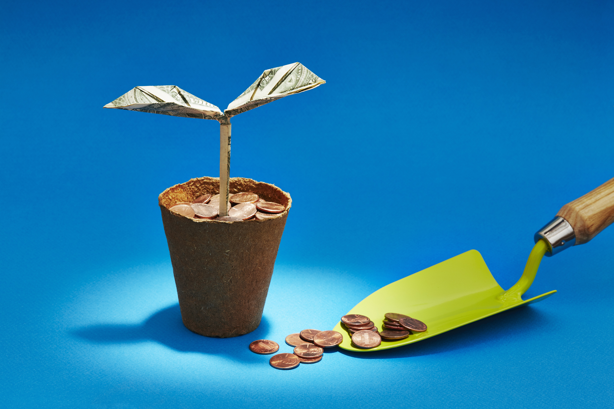 Origami dollar seedling growing in a flower pot of coins representing cash and investing in investment trusts