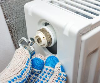 Someone turning a bleed valve on the end of a white, wall mounted radiator