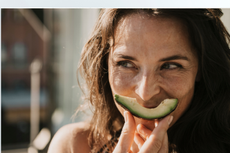 Woman with a slice of avocado in front of her face, so it look like a smile 