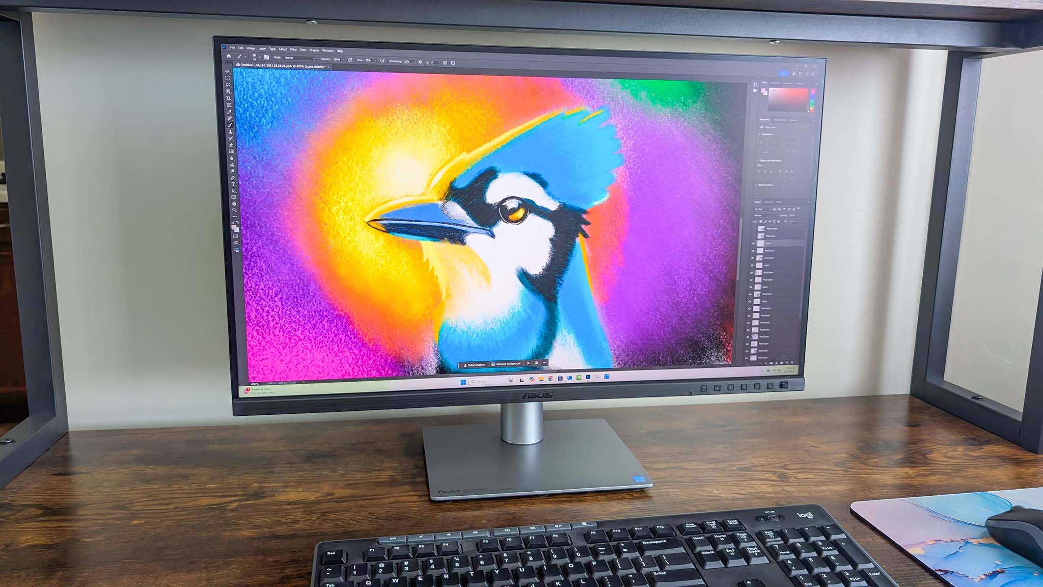 ASUS ProArt PA27JCV monitor on a desk and displaying Adobe Photoshop with a vibrant image of a bluejay.
