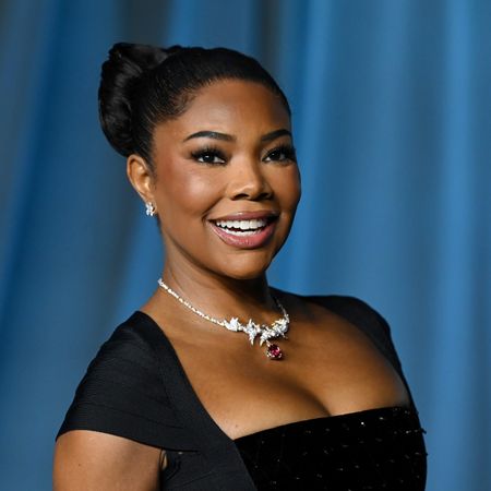 a black woman with dark hair poses on a red carpet in front of a blue background
