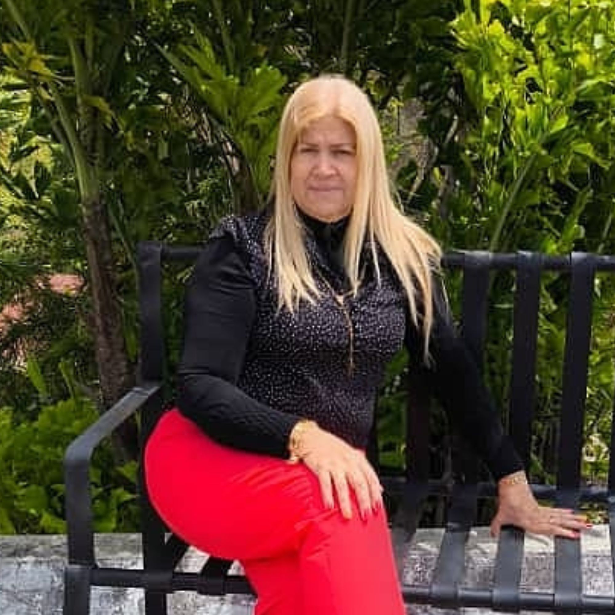 A picture of Veronica Smith sitting on an outdoor bench wearing red trousers and a black shirt.
