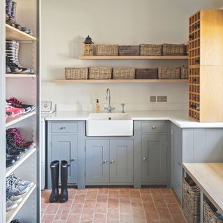 Boot room/utility room with blue cabinets and a sink, with wicker baskets on shelves above them