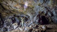 A person uses a flashlight to look up at the cave ceiling in a dark cave. 