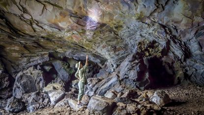 A person uses a flashlight to look up at the cave ceiling in a dark cave. 