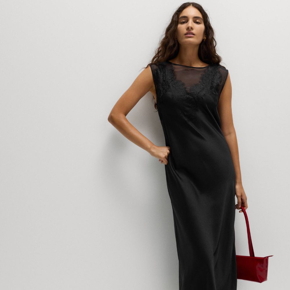 Model wears Marks and Spencer black slip dress with red bag and white kitten heel shoes.