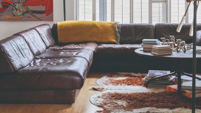 A living room with a large corner brown leather sofa with an animal hide rug and round coffee table in the middle