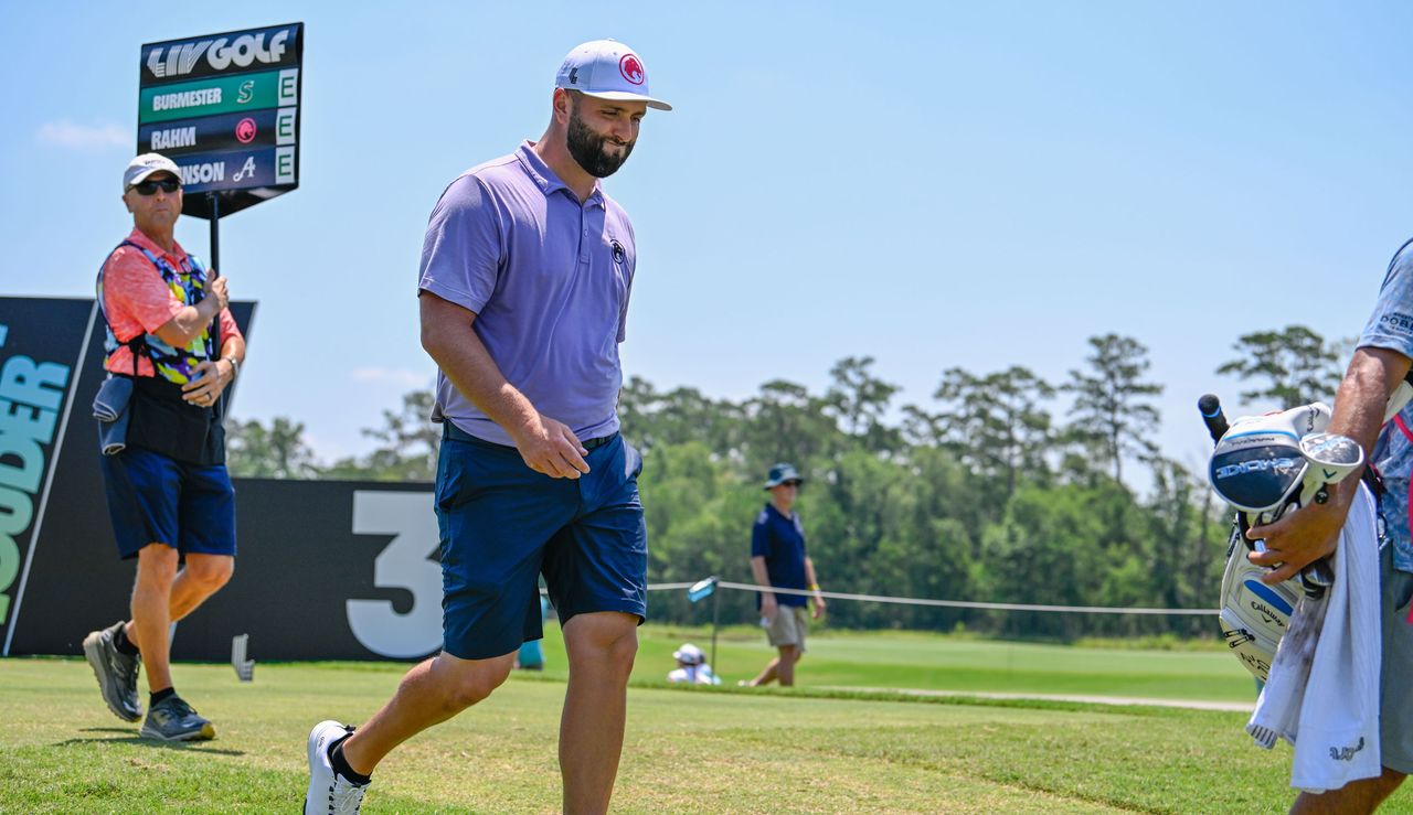 Jon Rahm walks off the third tee whilst grimacing 