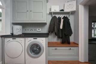 grey and wooden utility room and boot room design idea by lewis alderson, with coats hung up on hooks and a white washing machine and tumble dryer