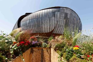 A flowery garden sits underneath a futuristic, silvery building.